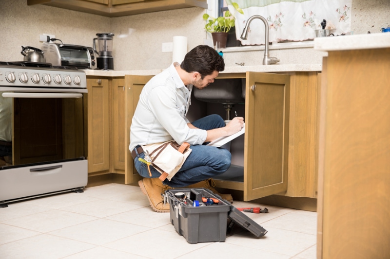 Plumber working underneath kitchen sink for plumbing house inspection.