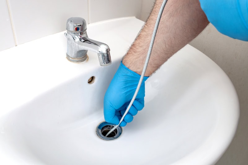 Why Do My Drains Keep Clogging? Photo of a hand snaking a drain.