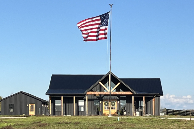 A photo of a new construction. House has black siding 4 windows out front, French entrance doors, and an American flag out front.