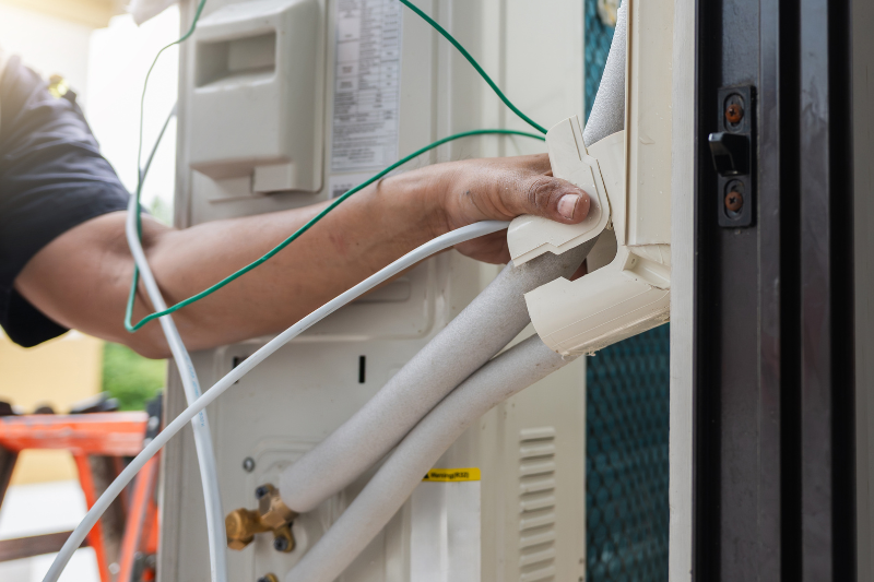 Image shows a technician plugging in an outdoor portion of a mini split HVAC unit. Mini split units are not single-stage.